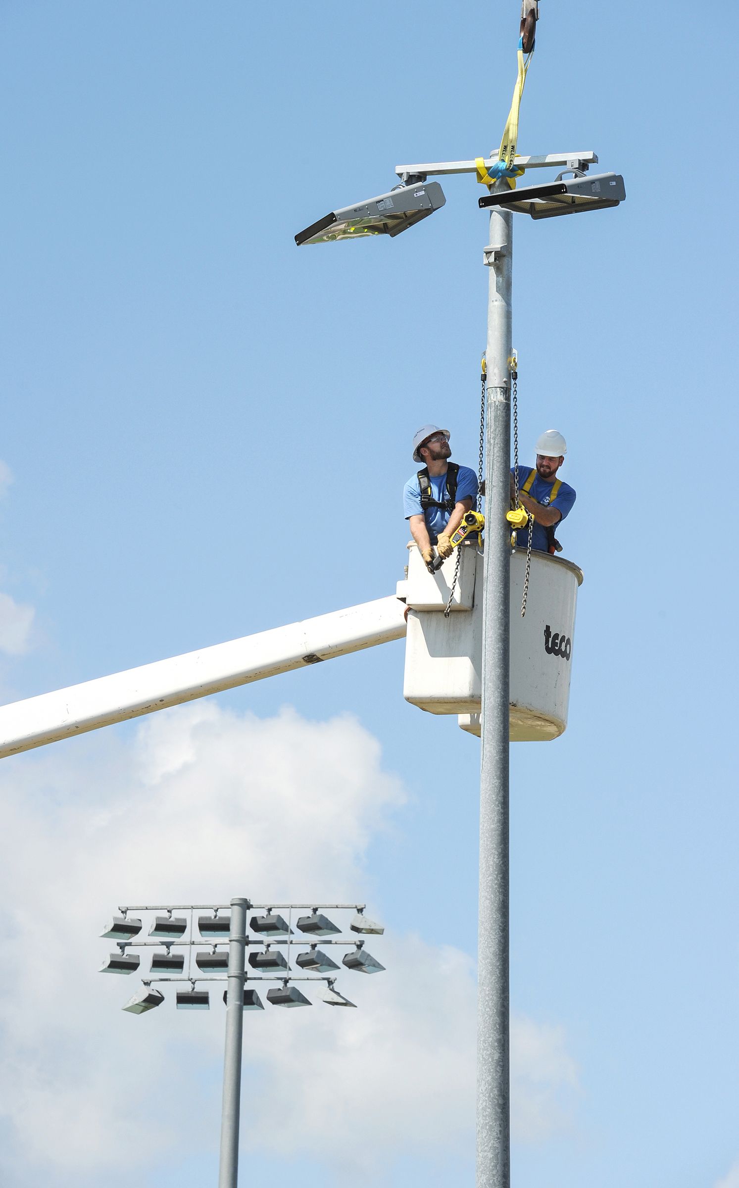 Two men are sitting in a bucket on top of a pole.