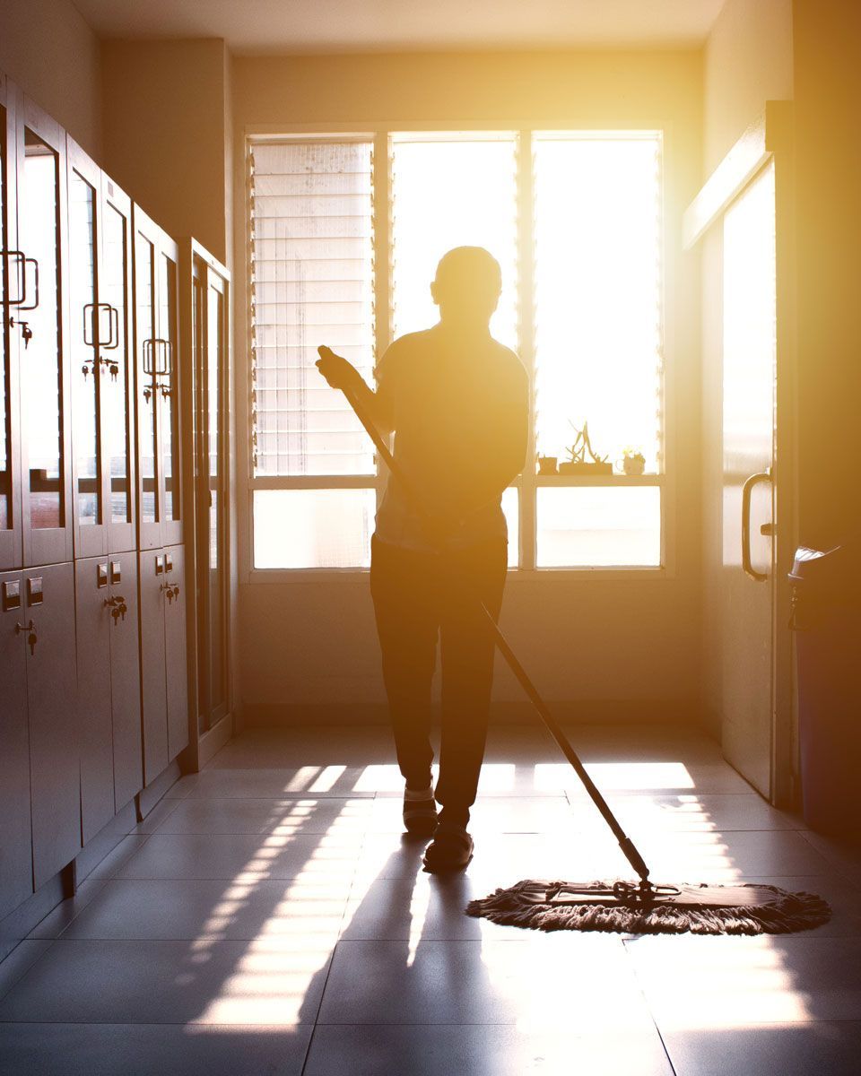 Person mopping a sunlit room with lockers, sunlight streaming through a window.