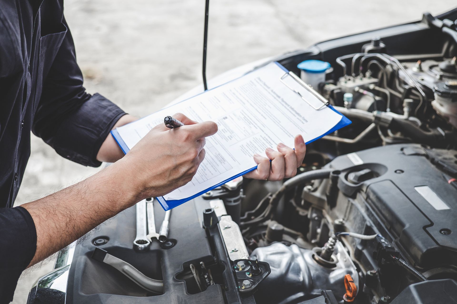 A man is writing on a clipboard while looking at the engine of a car.