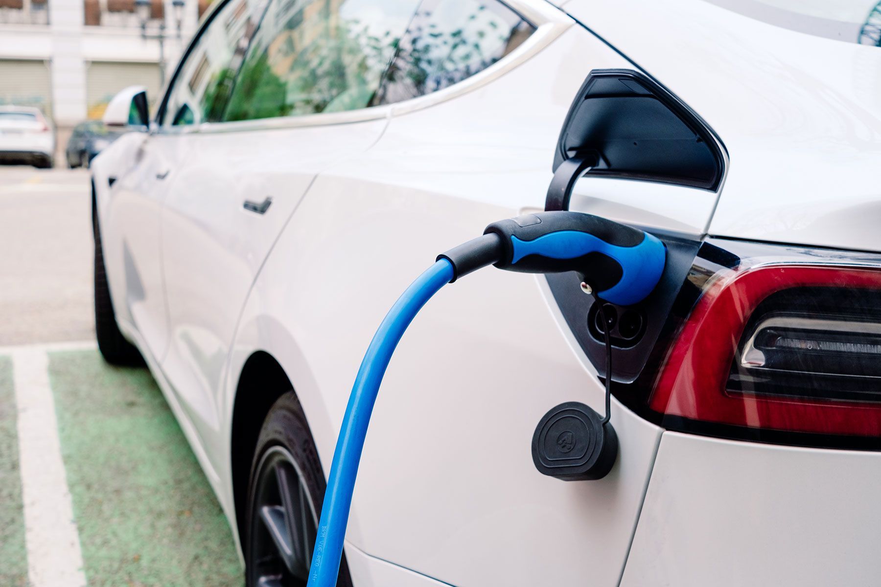 A white electric car is being charged in a parking lot.