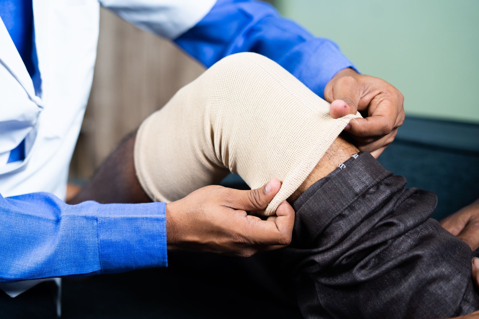 A medical professional applying an elastic compression bandage to a patient's knee.