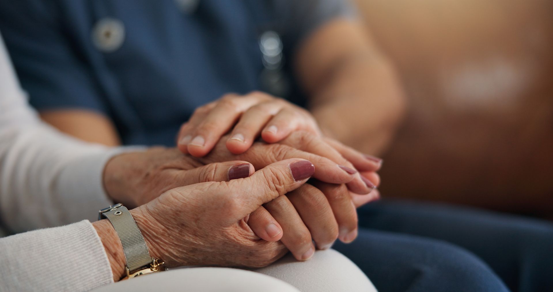 A close-up view of a person wearing a light-colored long-sleeved shirt holding the hands of a person wearing blue scrubs.