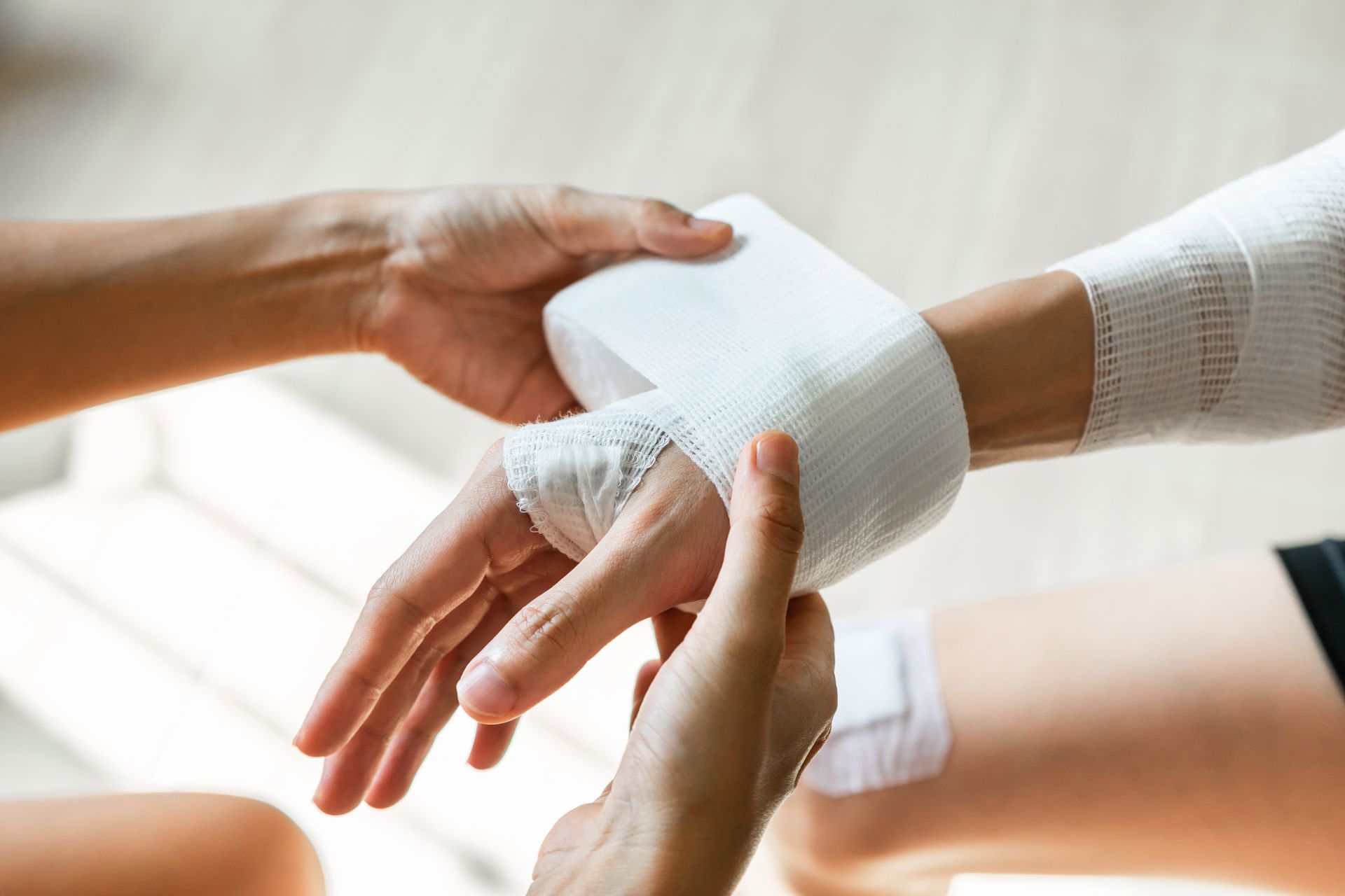 Hands applying a white compression bandage to another person's wrist.