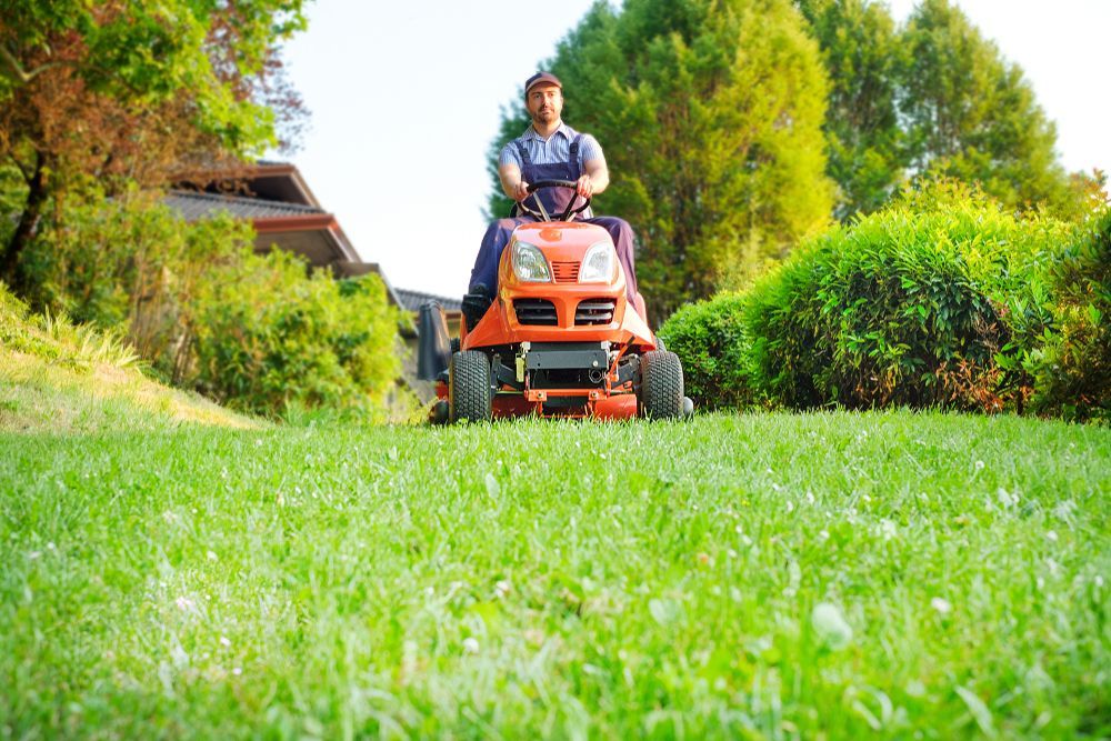 Man riding a red lawn tractor mowing a green lawn in a yard.