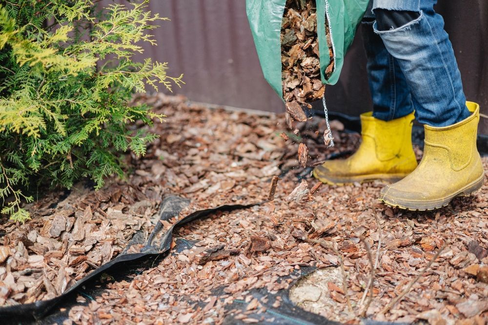 Person in yellow boots adding mulch to a garden bed.