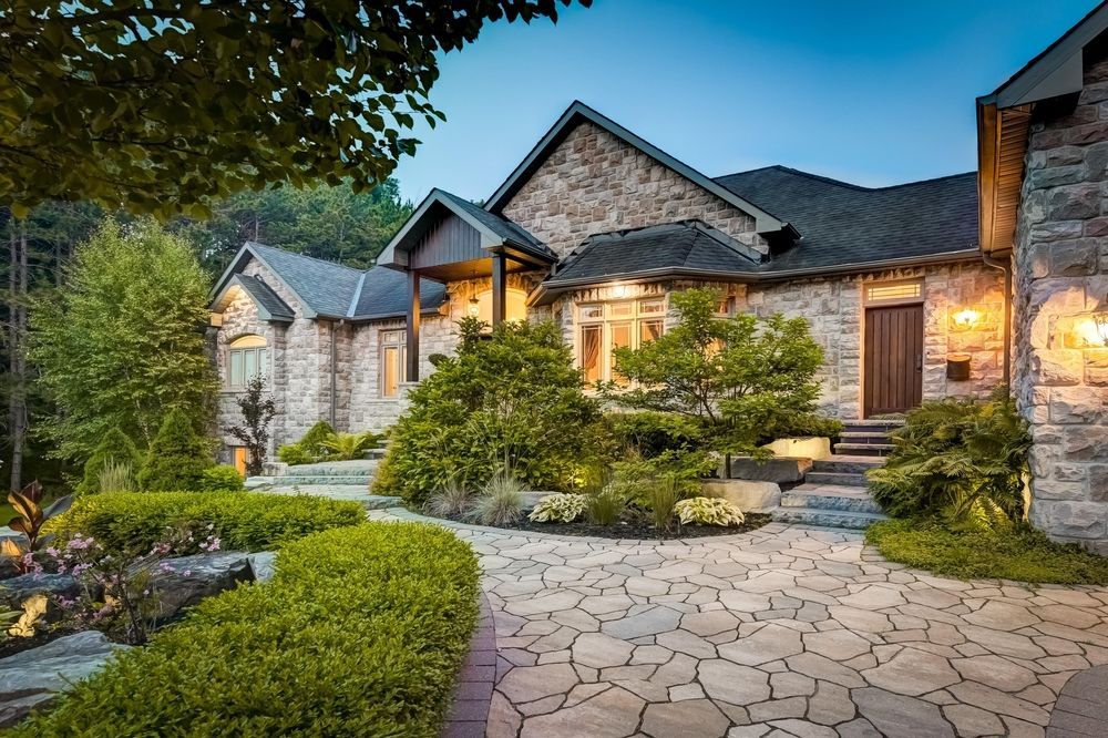 Stone house with landscaped front yard, stone walkway, and green shrubs.