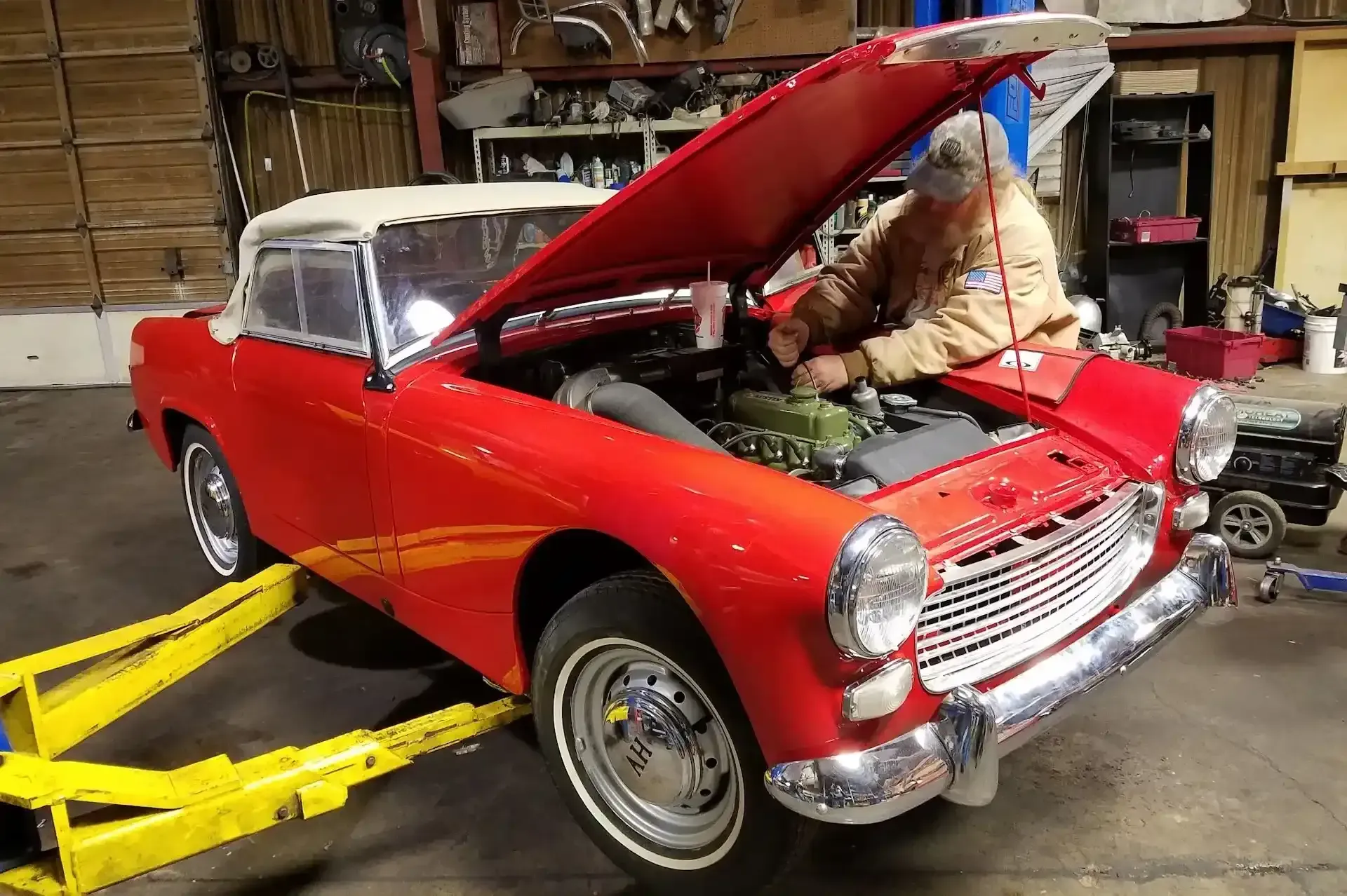 Man working on the engine of a red convertible car in a garage with the hood open. | Performance Auto Repair