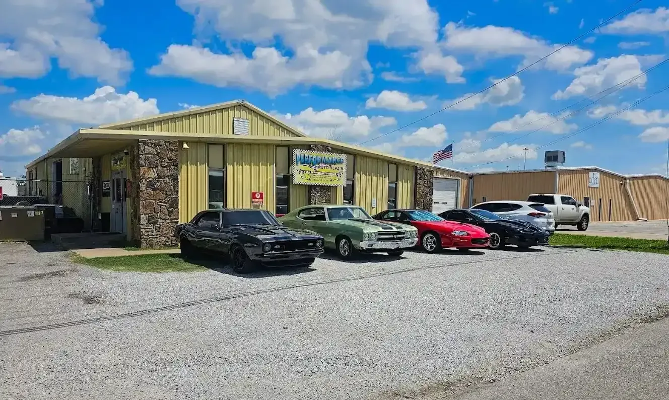 Yellow building with stone facade, bare tree, white SUV parked outside, dirt lot. | Performance Auto Repair