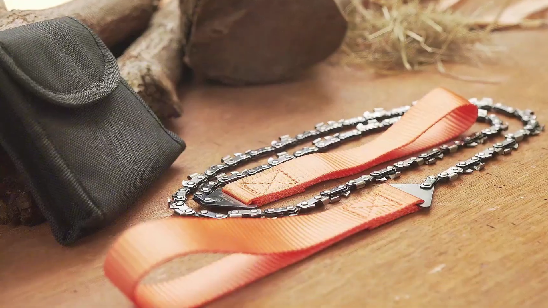 Pocket chainsaw with orange straps and a black case on a wooden surface.