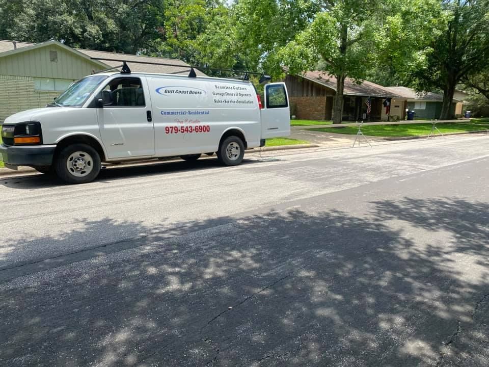 White van parked on a street with the side door open. The van has business information on the side.