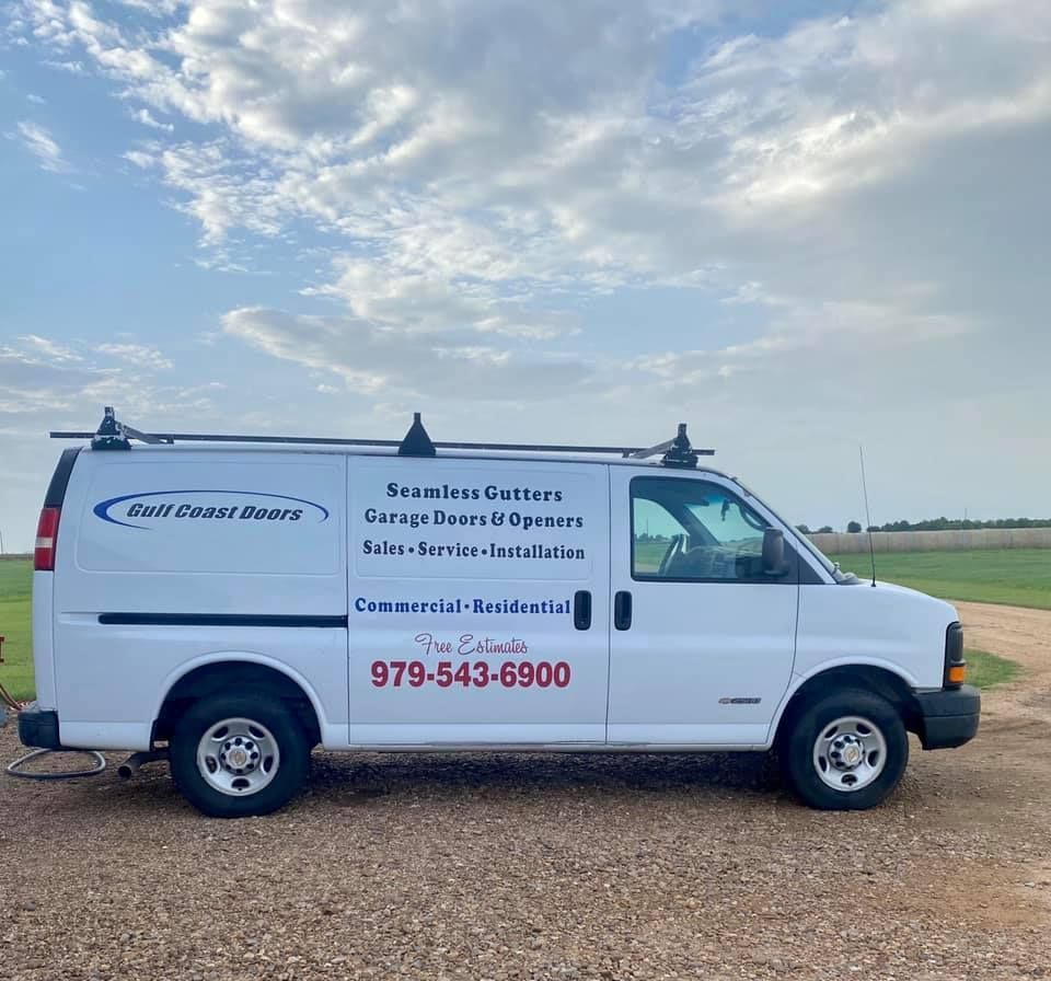 White work van with logo for Gulf Coast Doors parked on gravel. Cloudy sky in the background.