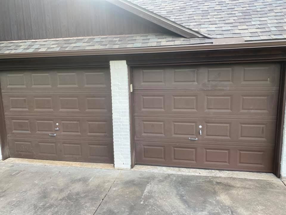 Two brown garage doors, side-by-side, under a brown roof and a white brick support column.