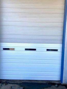 White roll-up garage door, partially open. Horizontal ridges, three small windows in bottom section.