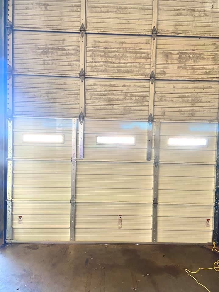 White industrial garage door with three sections, three windows, and distressed top panels.