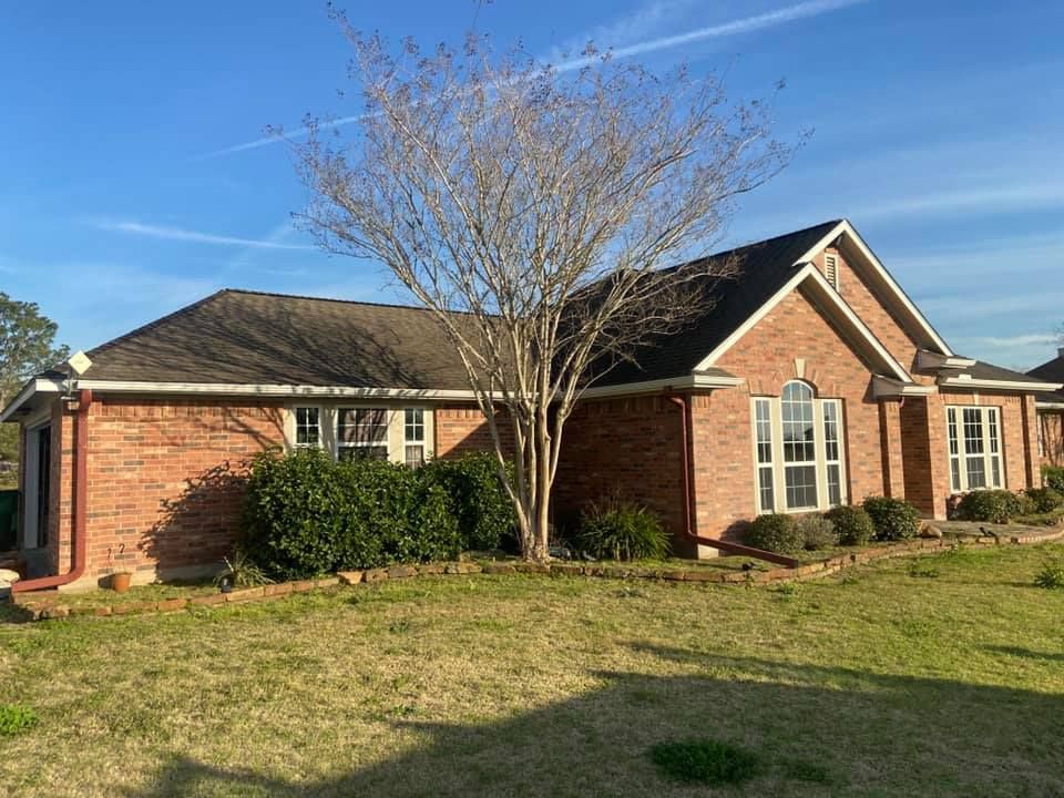 Red brick house with brown roof and bare tree in front yard. Blue sky.
