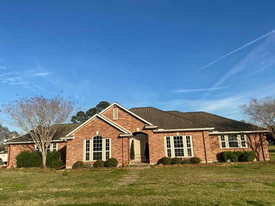 Brick house with a dark roof and multiple windows under a blue sky.