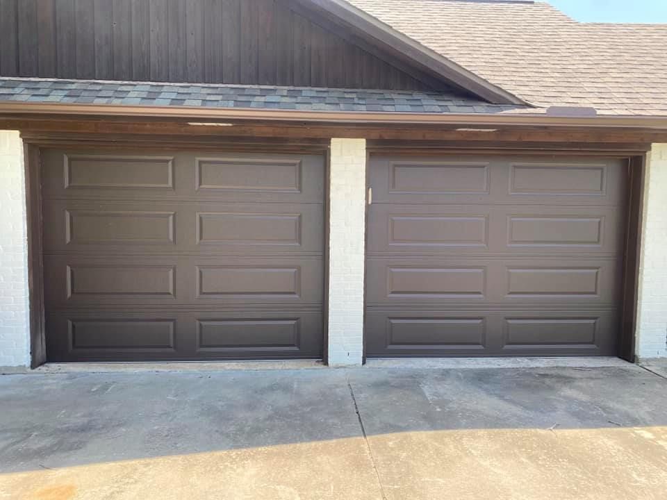 Two brown garage doors on a gray concrete driveway, under a brown roof.