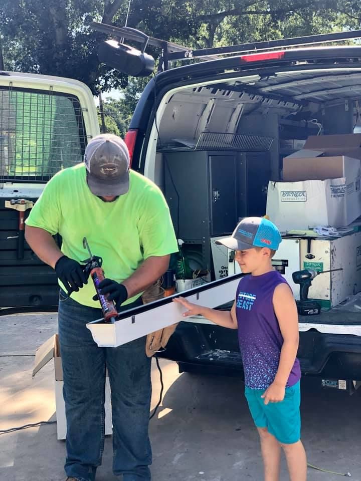 Man in neon shirt using sealant with a child near an open van.