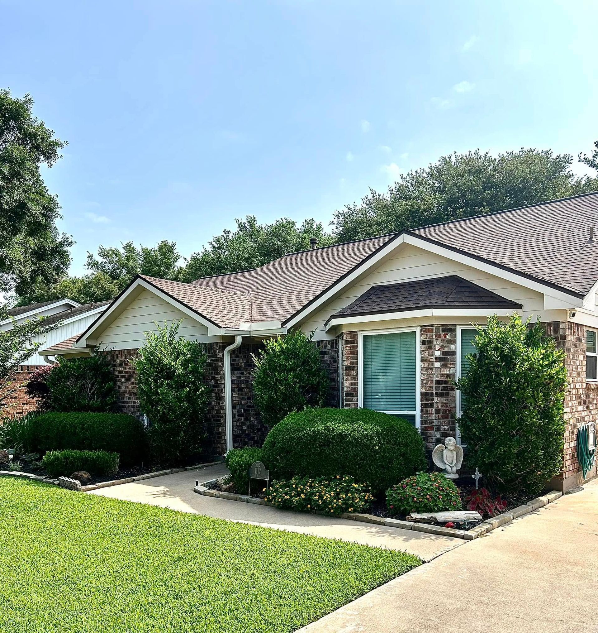 Single-story brick house with manicured landscaping, brown roof, and a clear blue sky.