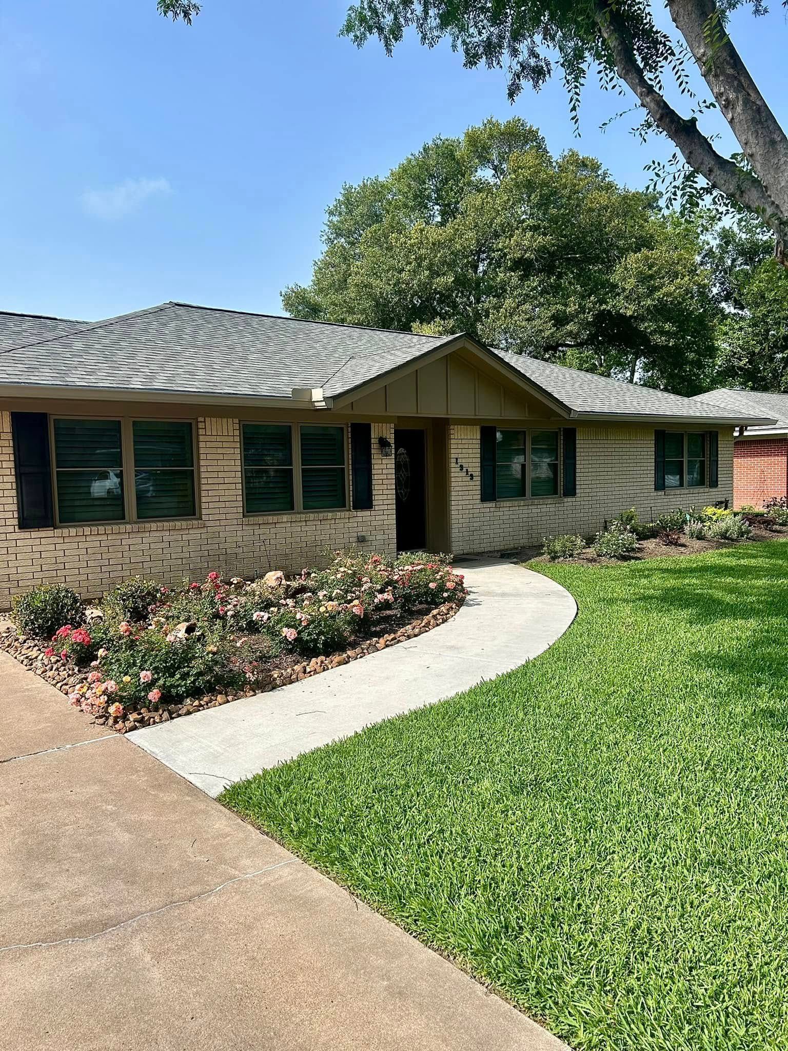 Brick house with a curved sidewalk, lawn, and flower beds under a blue sky.