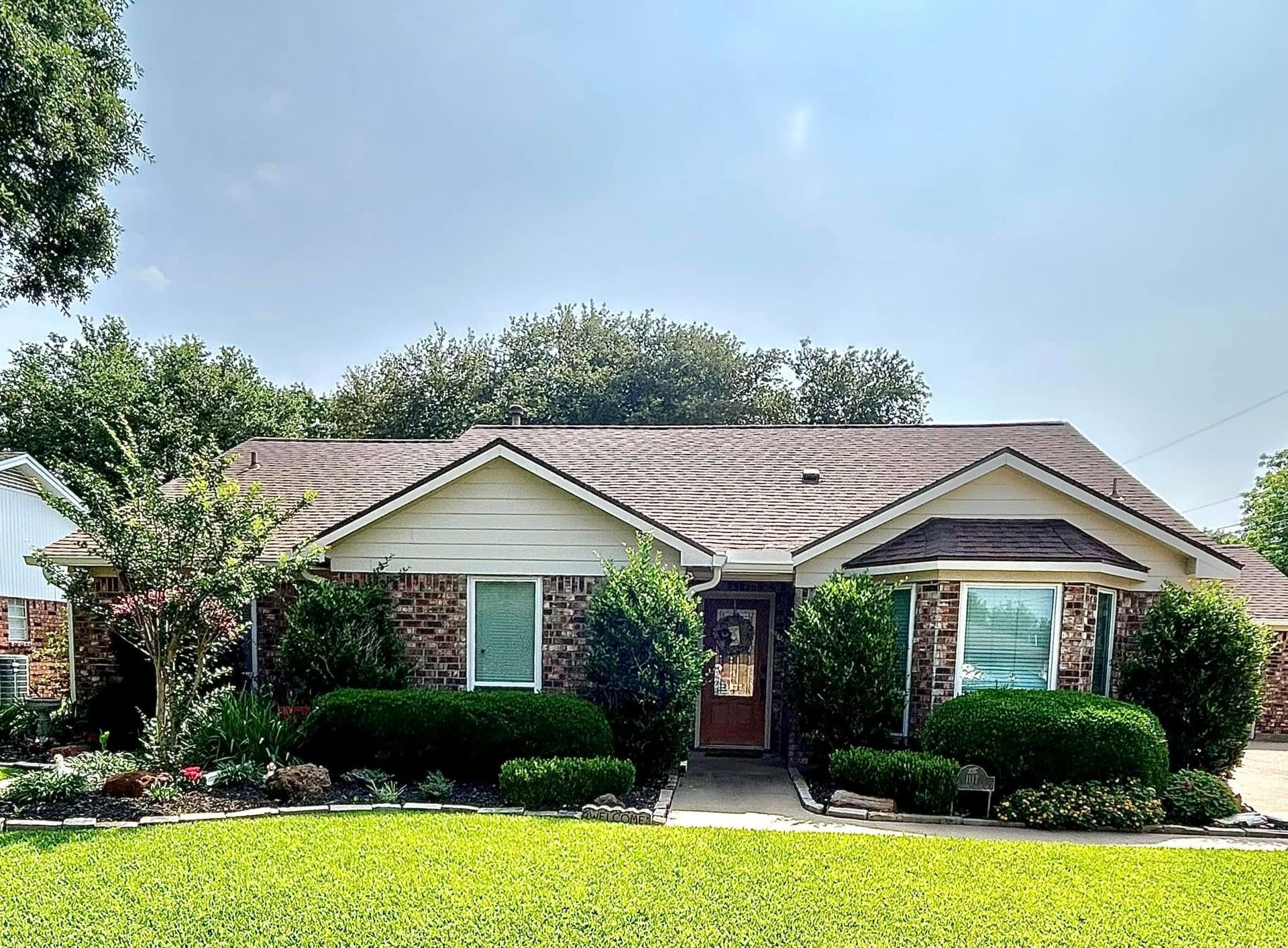 Single-story brick house with green lawn, landscaping, and a blue sky in the background.