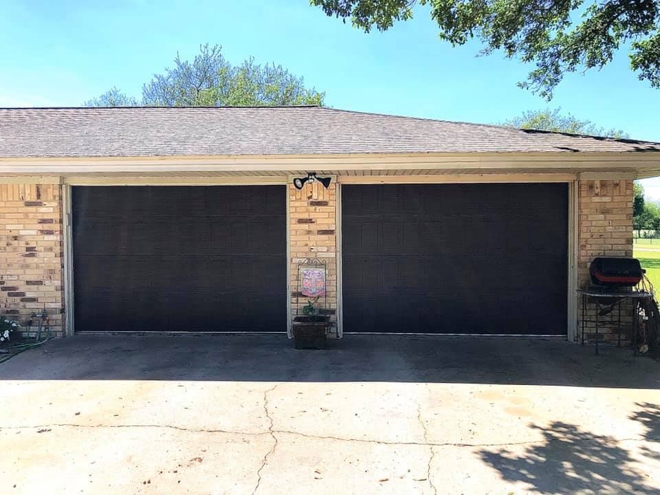 Two black garage doors on a brick house with a concrete driveway, under a clear blue sky.