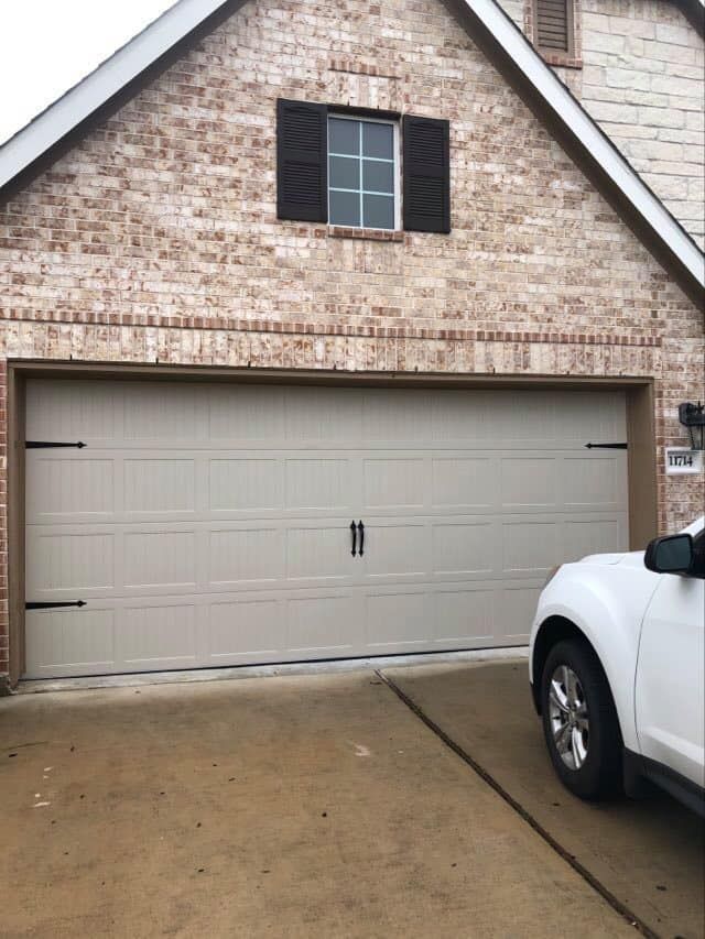 Tan garage door on a brick house with a white SUV parked in the driveway.