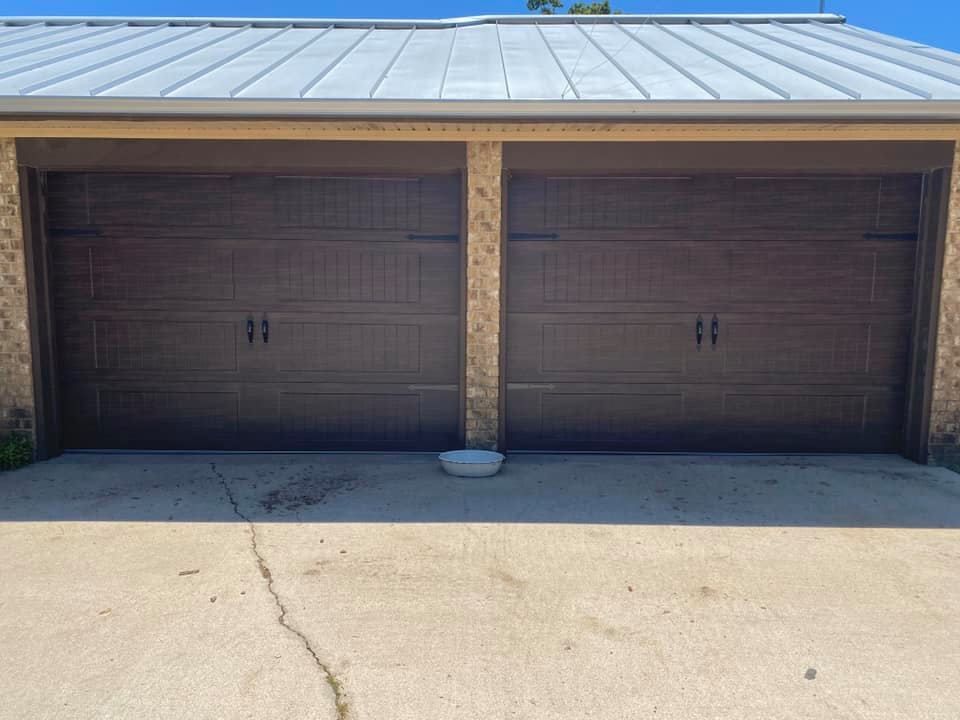 Two dark brown garage doors with metal roof above, on a concrete driveway.