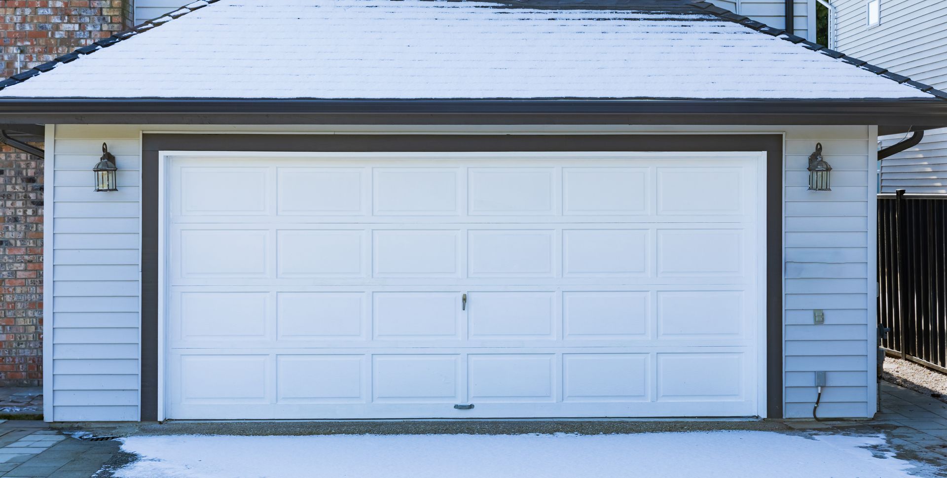 White garage door on a snow-covered building with lights, and dark trim.