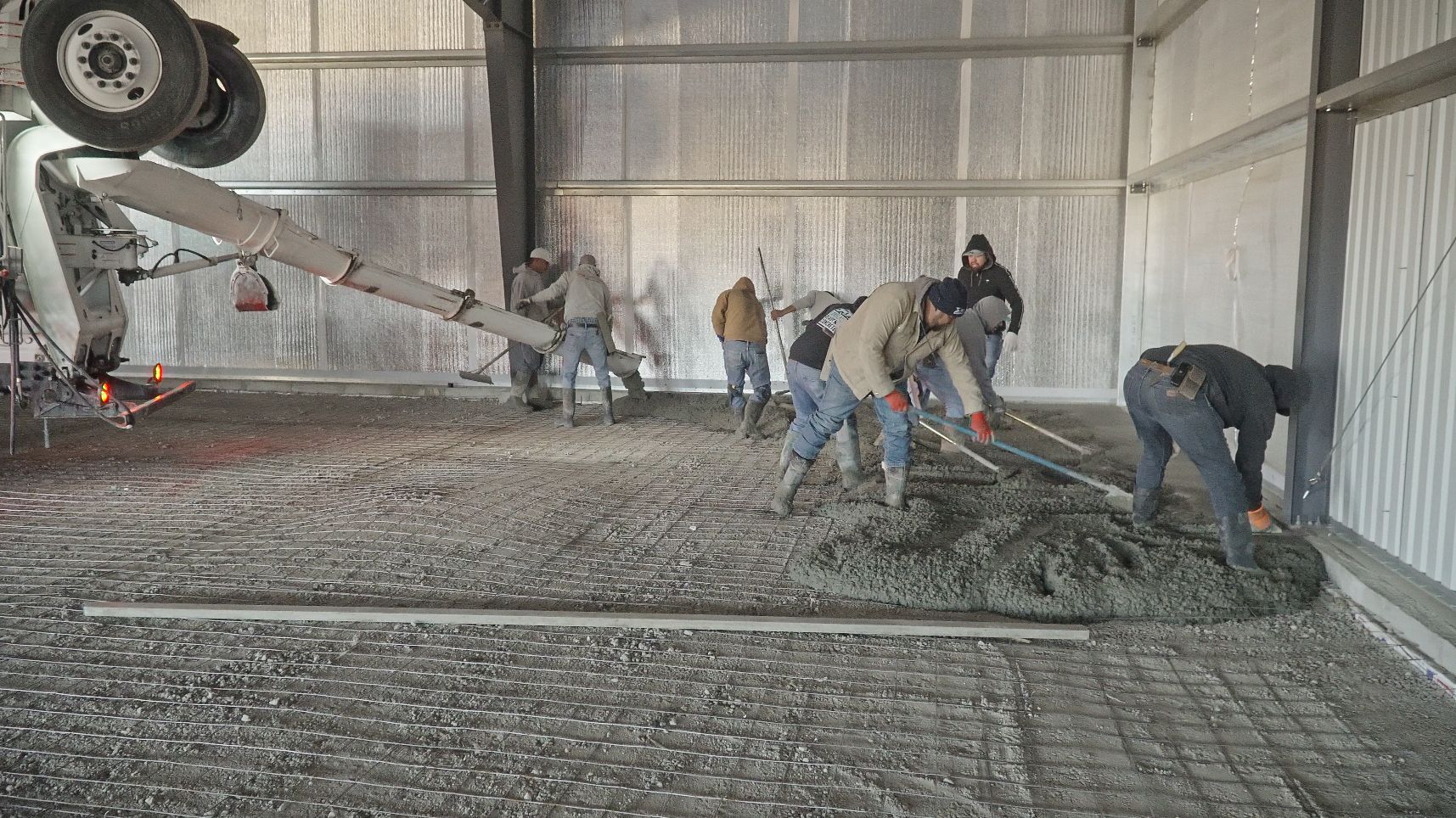 Concrete pouring into wooden forms on a construction site; workers in safety vests.