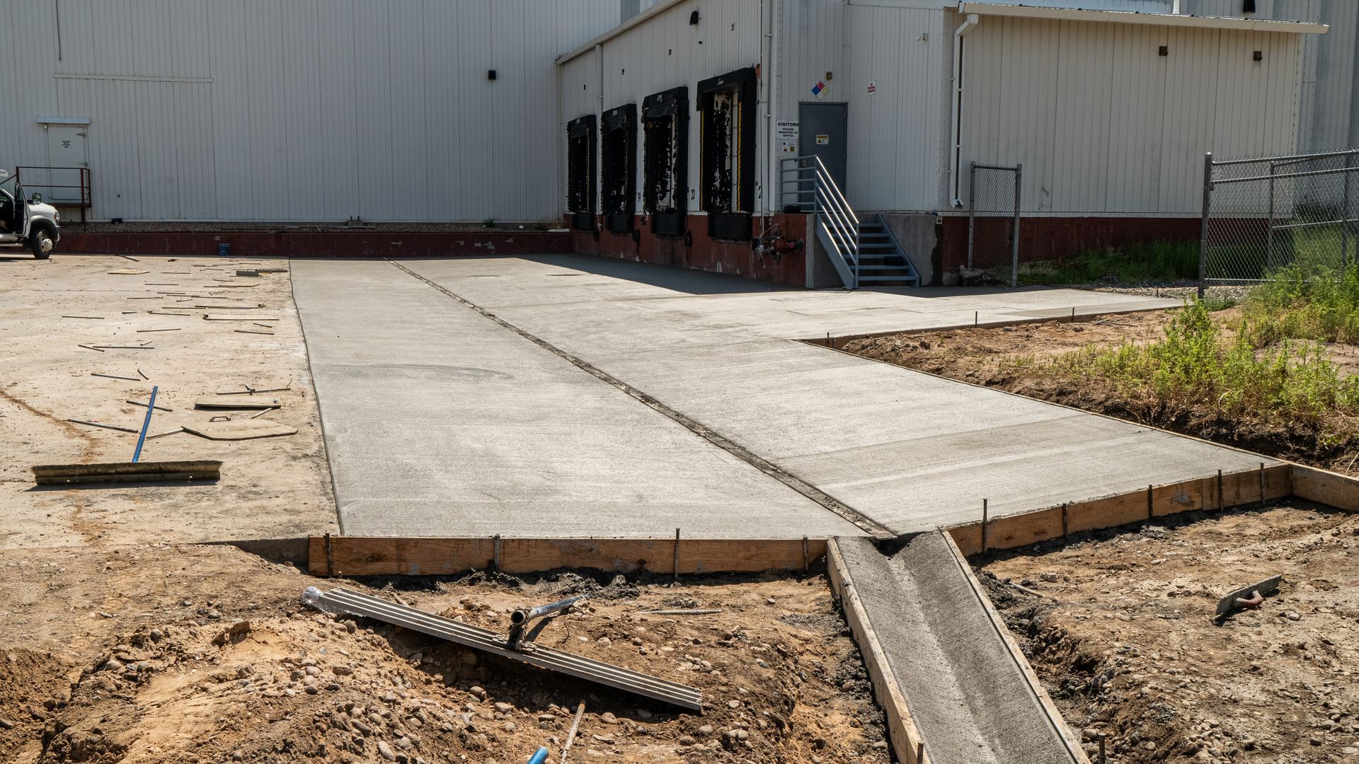 Gray house with a concrete driveway and wooden fence, under a cloudy sky.