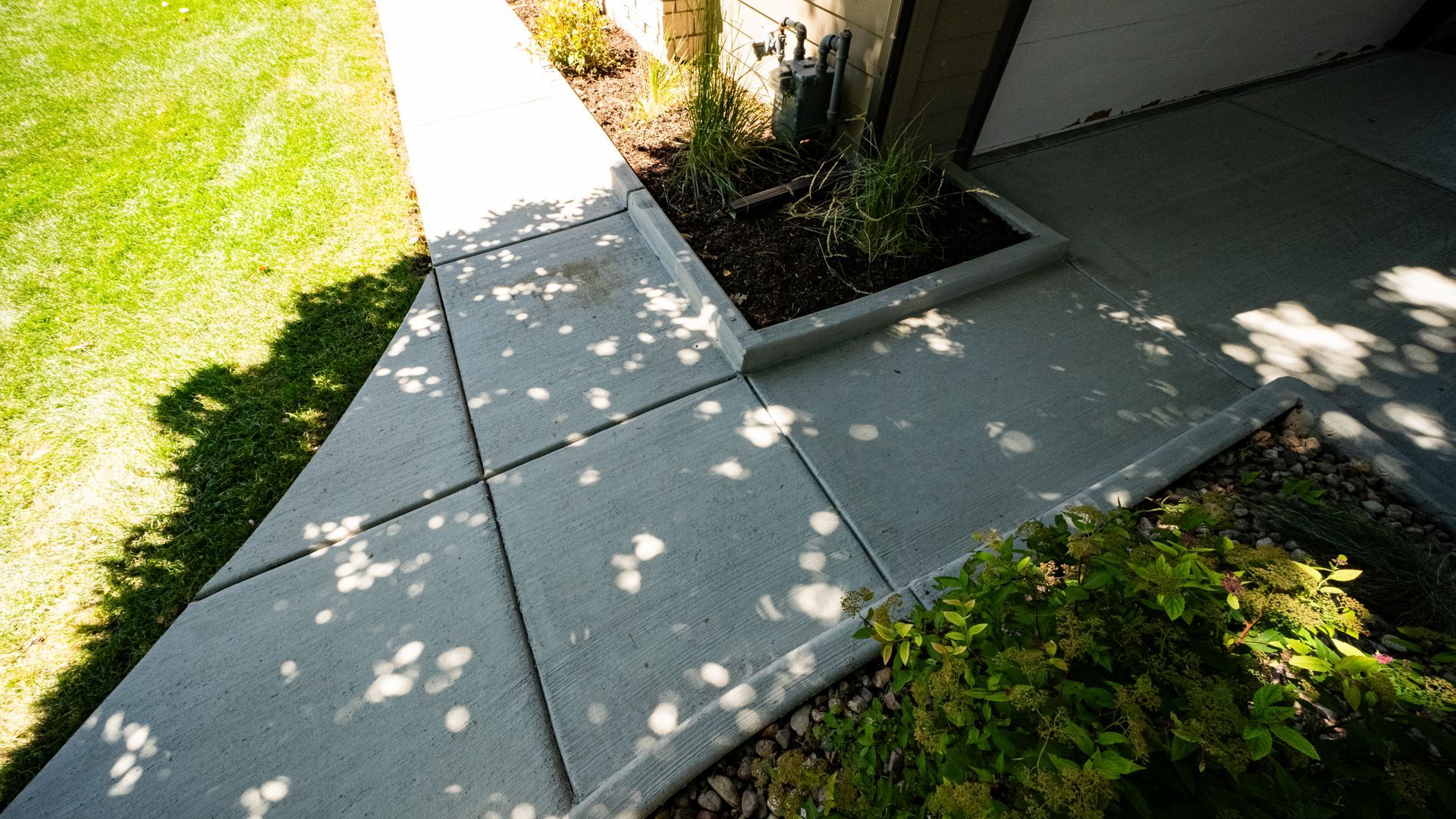 Curving concrete pathway in a garden, edged with green shrubs and grass. Sunny setting.
