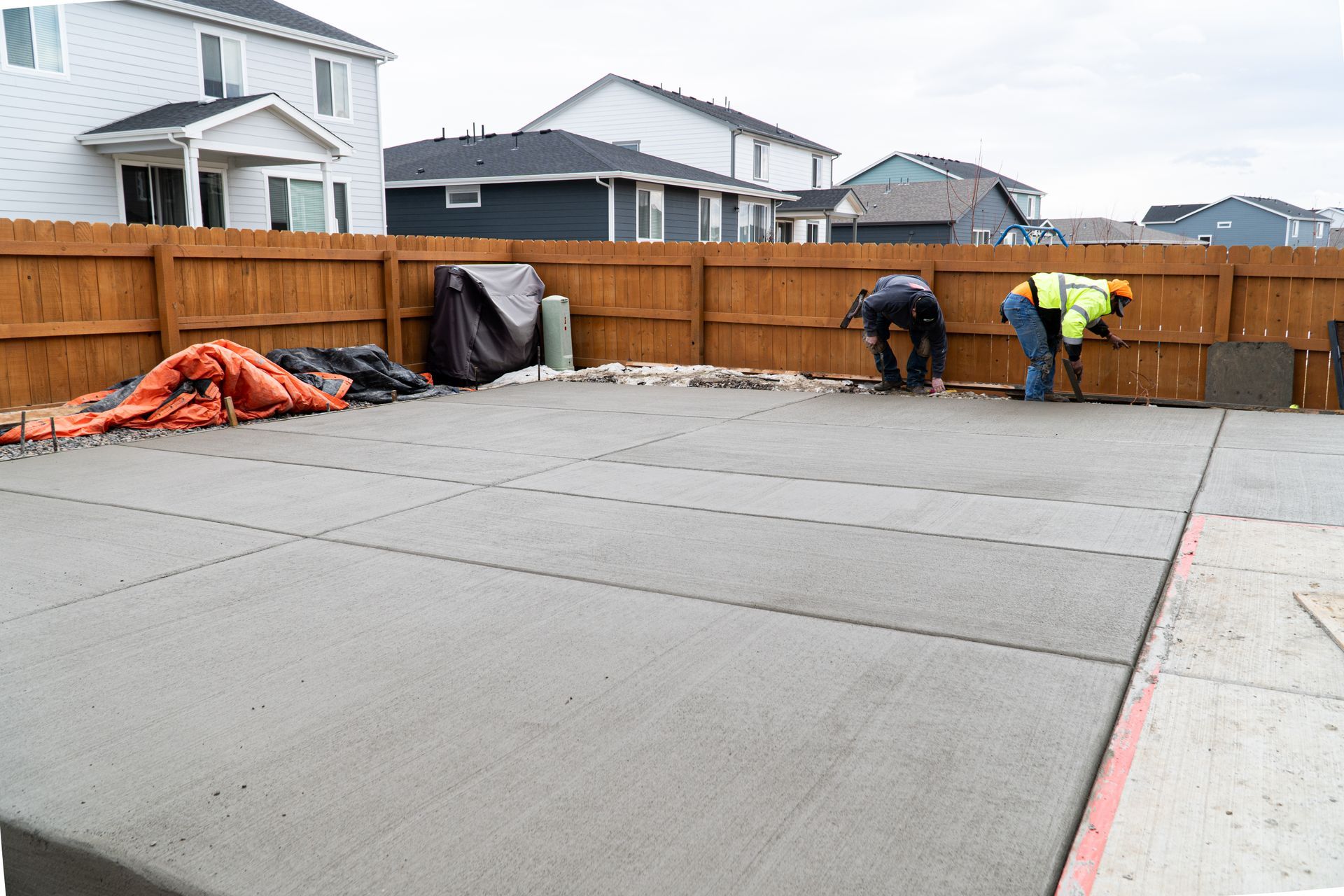 Gray house with a concrete driveway and wooden fence, under a cloudy sky.