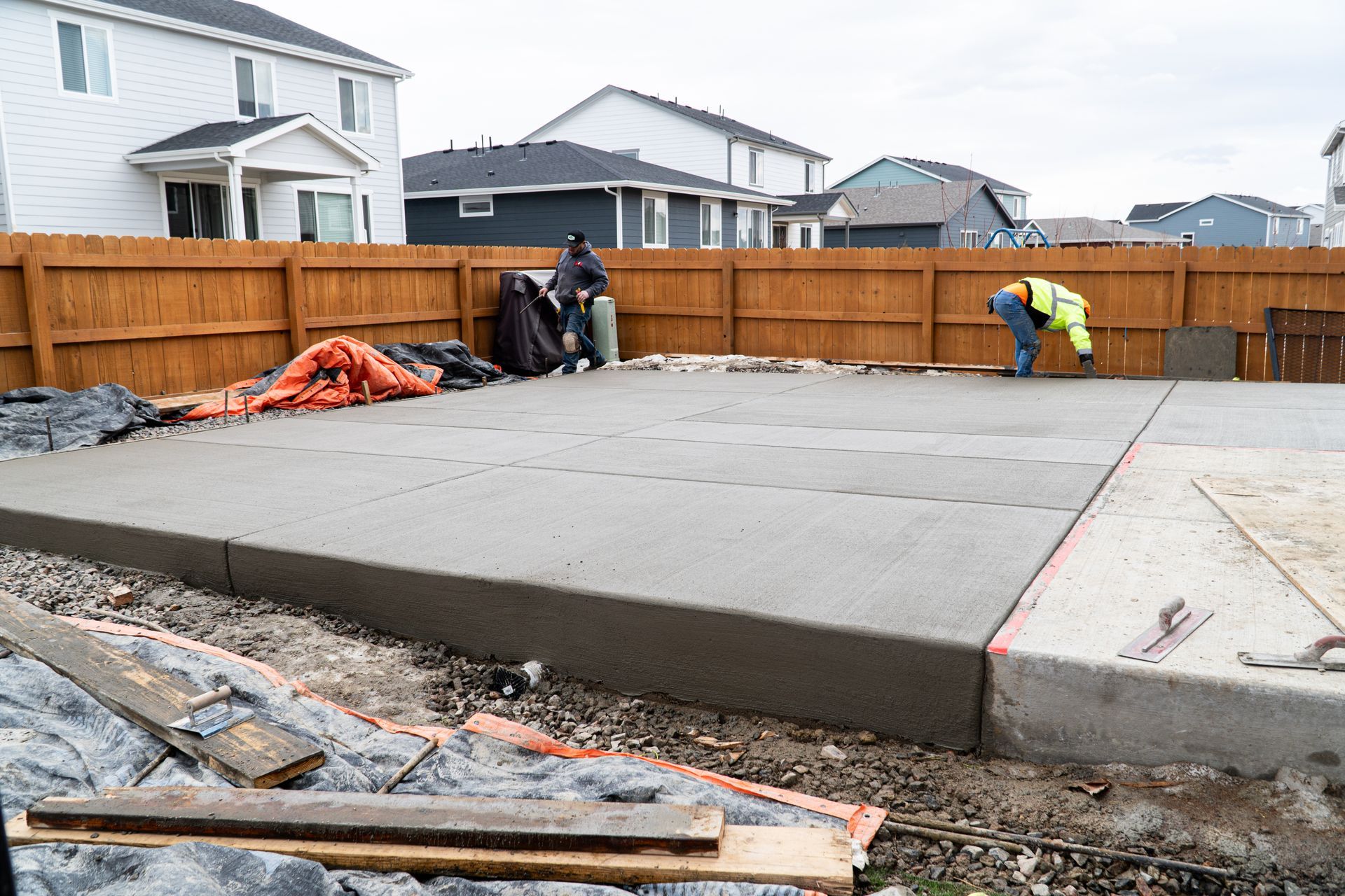 Construction worker in neon vest bends over concrete slab, working on a construction site.