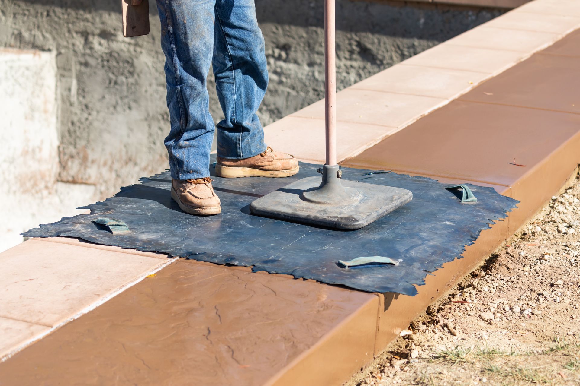 Person using a tool to smooth concrete on a brown, rectangular surface. Feet are on a dark mat.