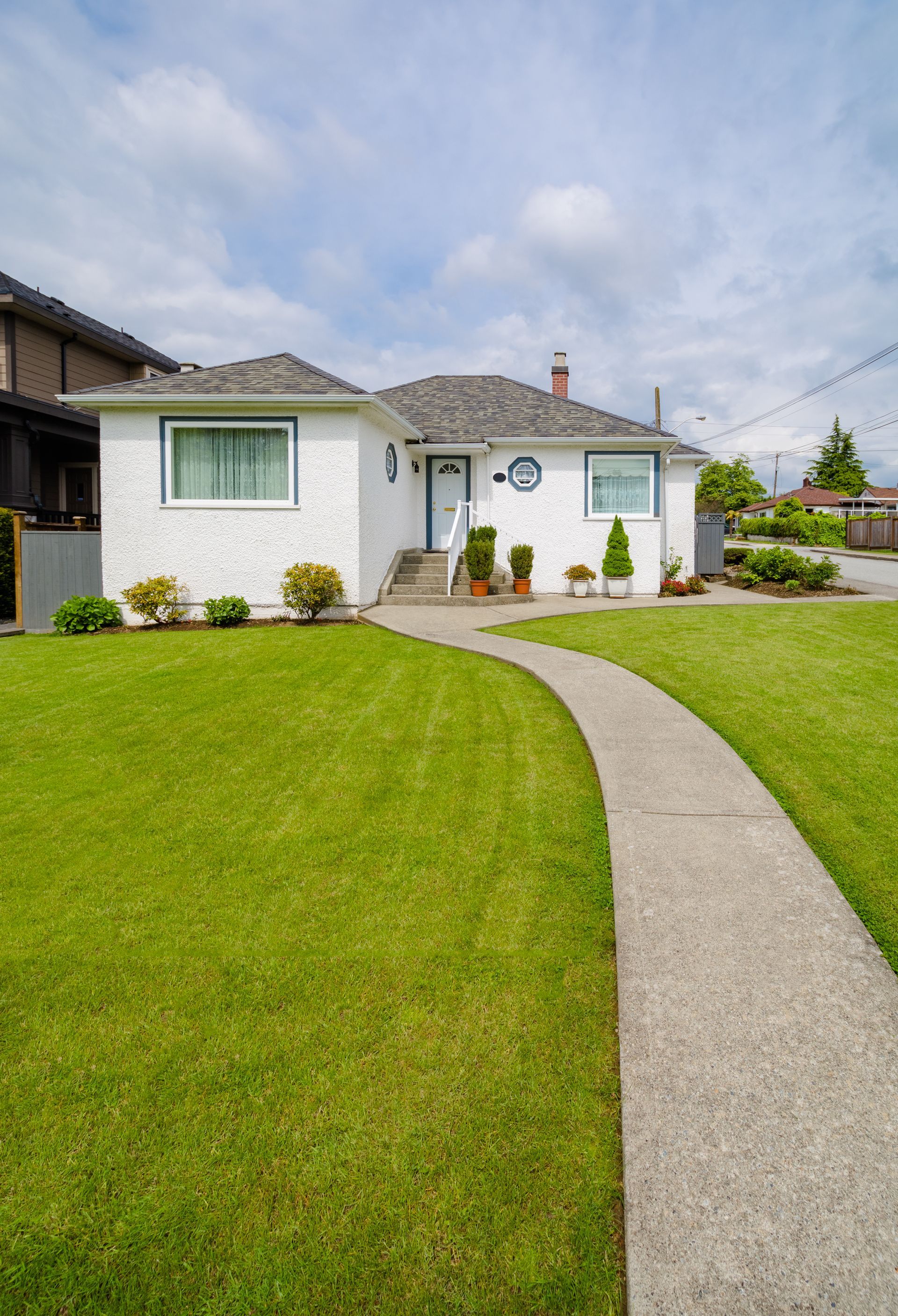 White house with green lawn, curved sidewalk, and blue sky.