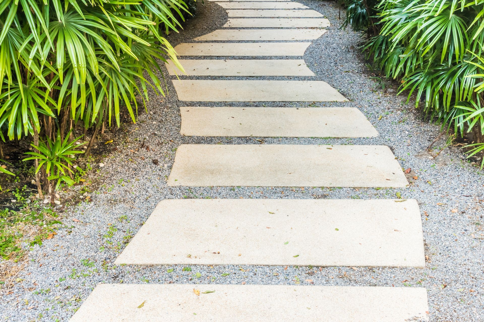 Stone path winds through a garden, lined with greenery and gravel.