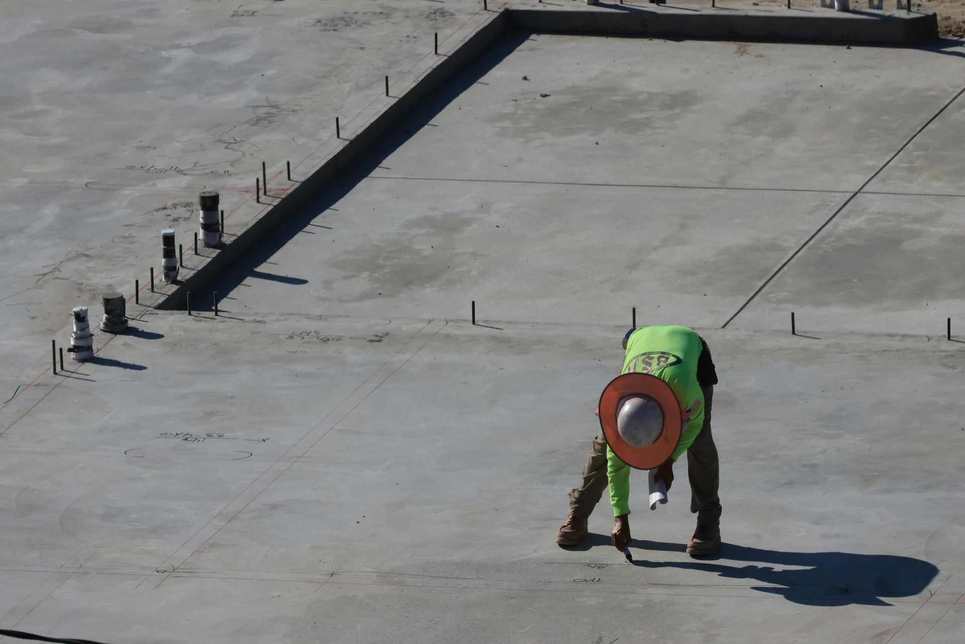 Construction worker in neon vest bends over concrete slab, working on a construction site.
