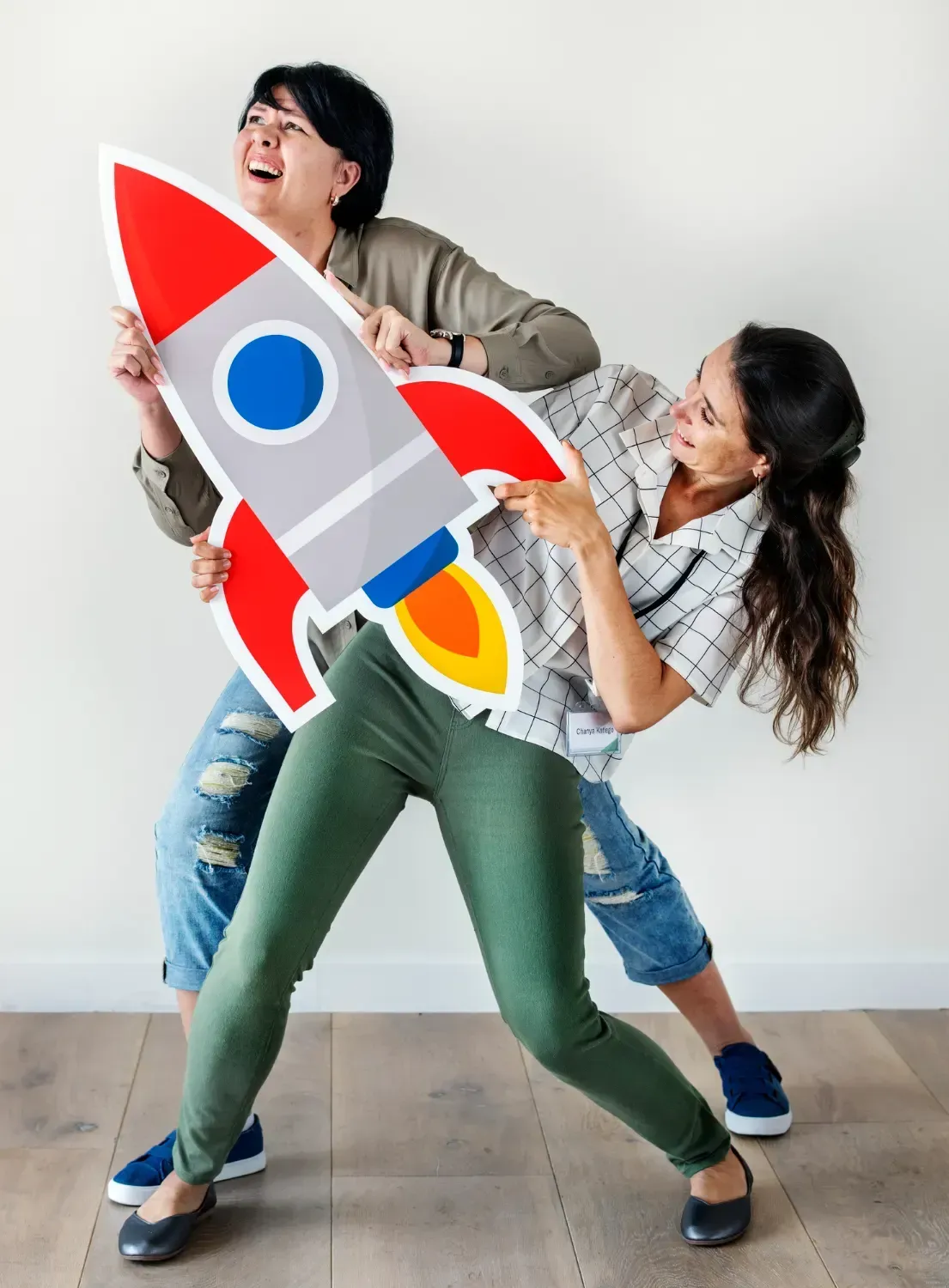 Two women are holding a cardboard rocket in their hands.