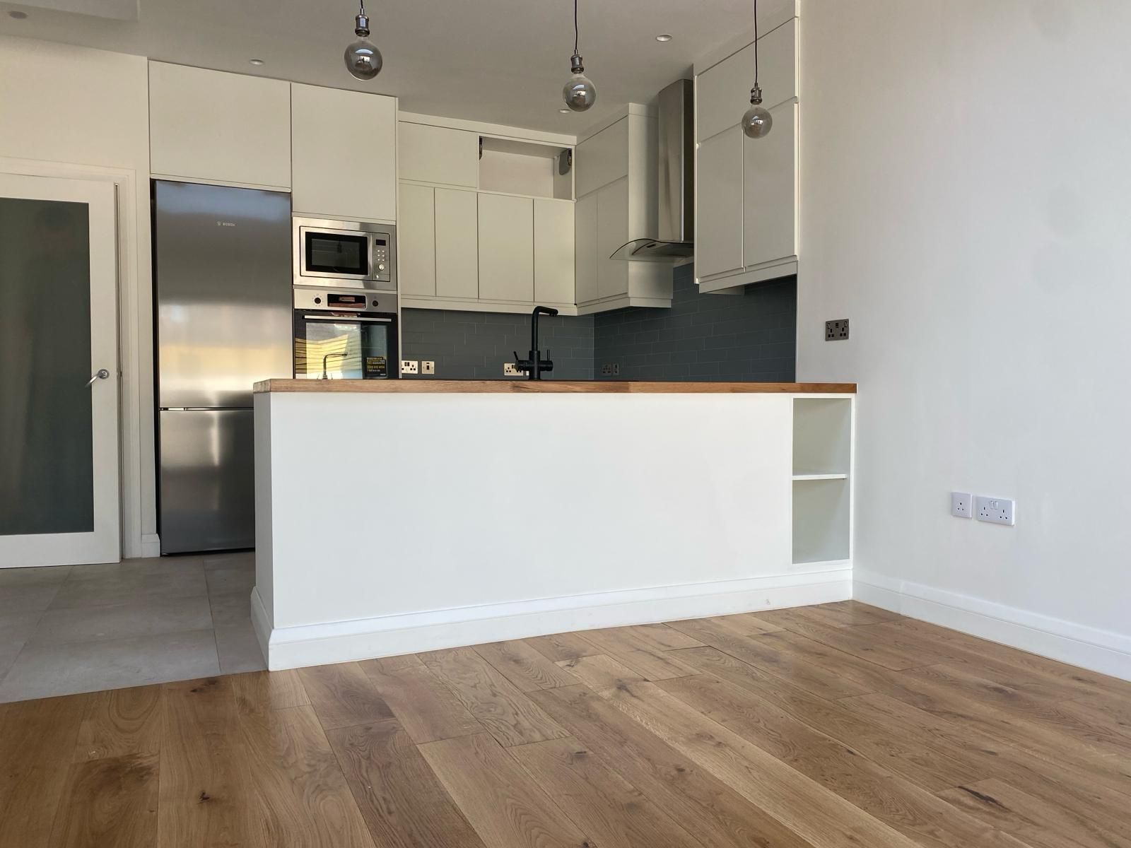 an empty kitchen with white cabinets and wooden floors