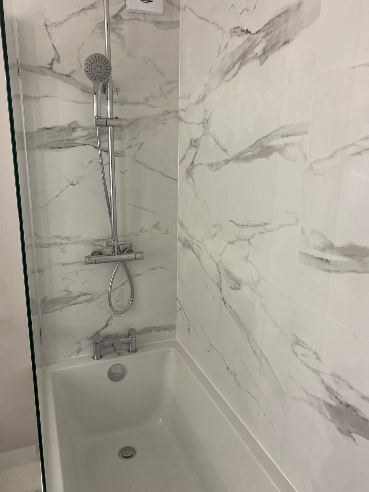 a bathroom with marble tiles and a bathtub with a shower head .