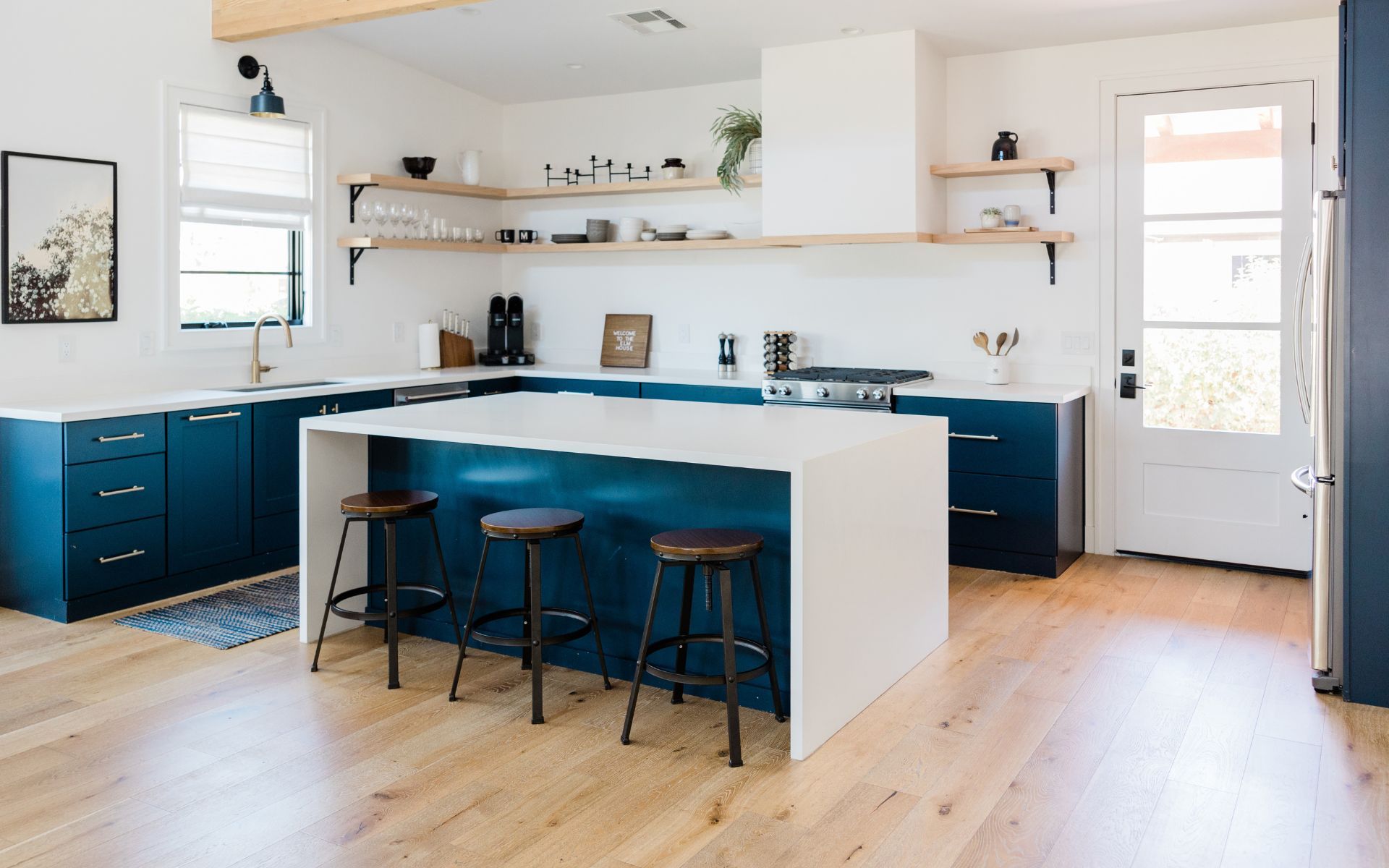 a kitchen with blue cabinets , white counter tops , and wooden floors .
