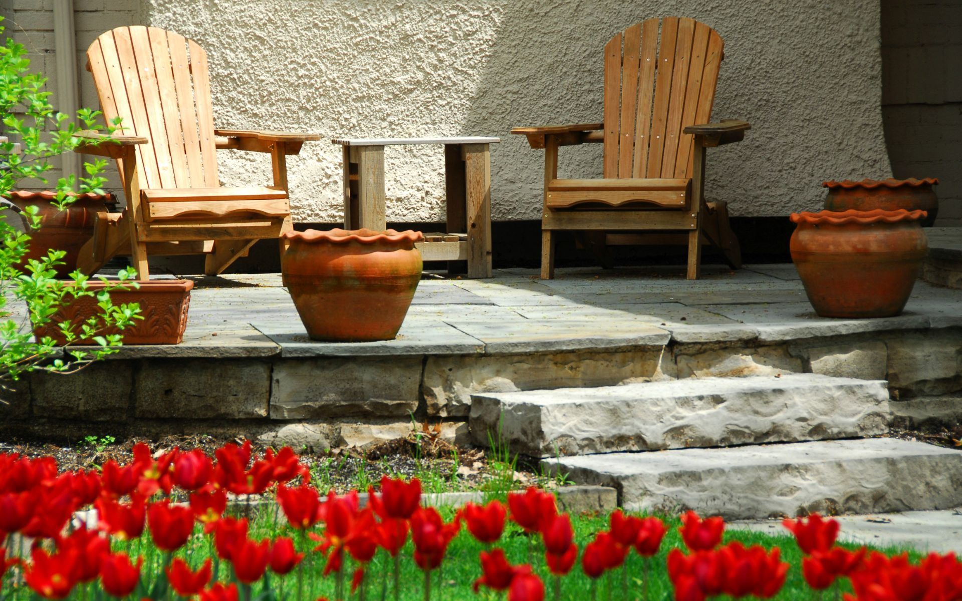 a patio with two wooden chairs and potted plants