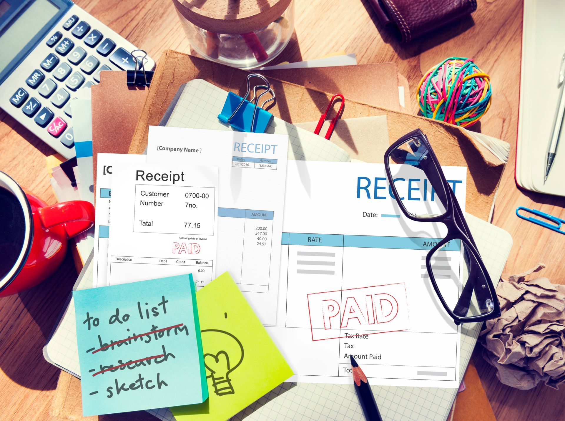 A desk with a receipt , a cup of coffee , a calculator , and sticky notes on it