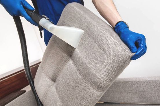 A Person is Cleaning a Couch With a Vacuum Cleaner — Tailored Services in Mackay Harbour, QLD