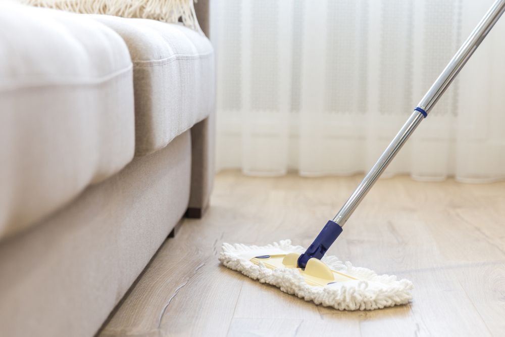 A Mop Is Being Used To Clean A Wooden Floor In A Living Room — Tailored Services in Proserpine, QLD