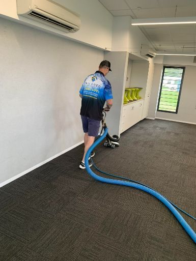 A Man Is Cleaning A Carpet With A Vacuum Cleaner In A Room — Tailored Services in Mackay Harbour, QLD