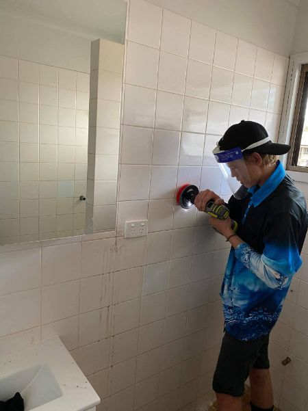 A Man Is Cleaning A Bathroom Wall With A Brush — Tailored Services in Mackay Harbour, QLD