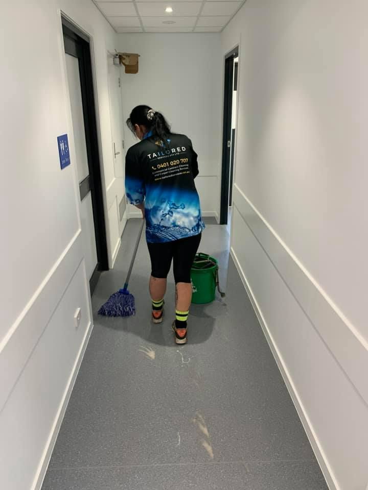 A Woman Is Cleaning A Hallway With A Mop And Bucket — Tailored Services in Mackay Harbour, QLD
