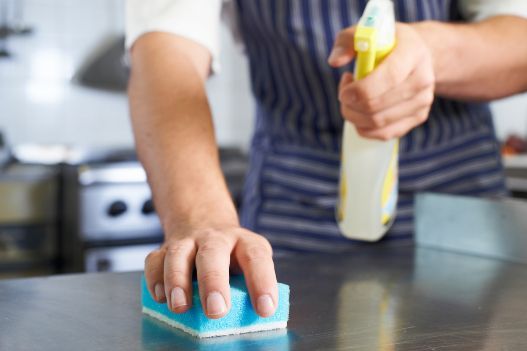 A Person is Cleaning a Counter With a Sponge and Spray Bottle — Tailored Services in Walkerston, QLD